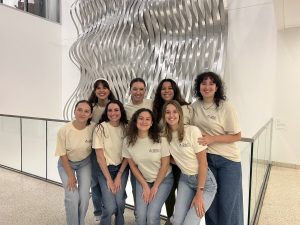 A group of college students pose for a photo in front of a silver modern sculpture.